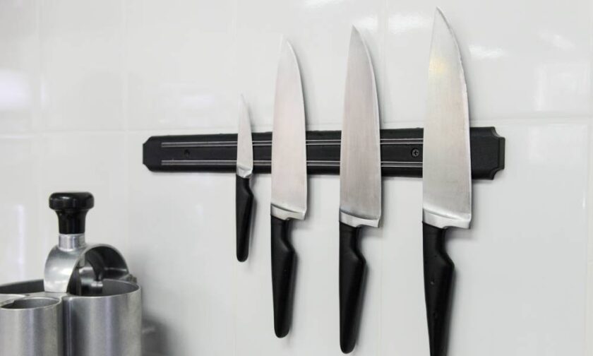 Four knives varying in length and width that are attached to a magnetic surface that is hanging on the wall.