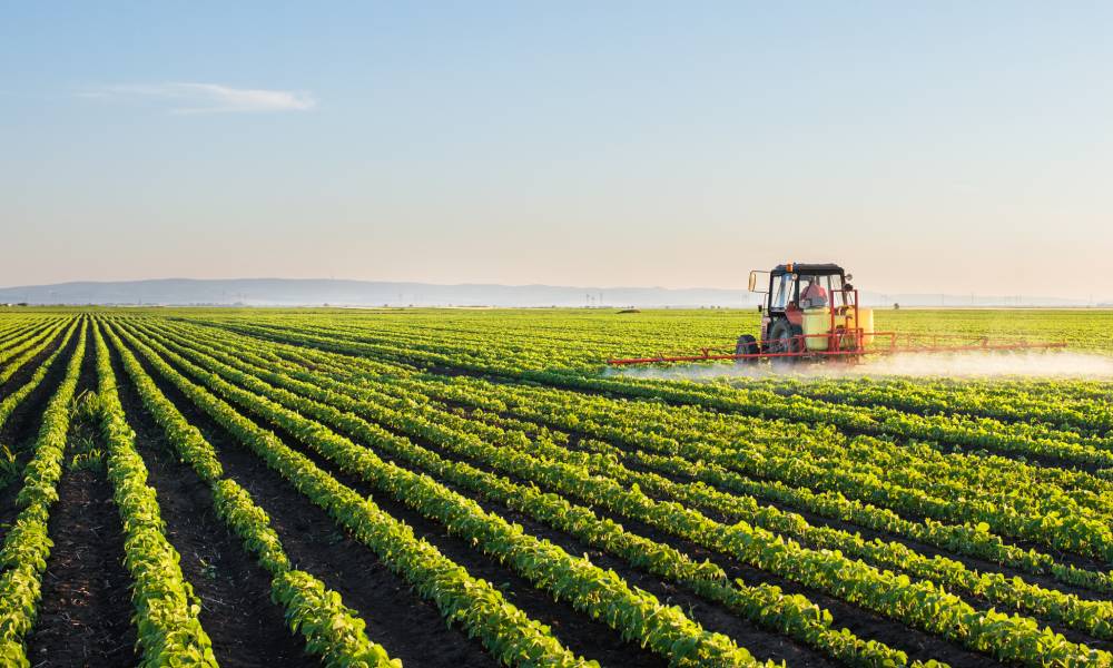 A large, red tractor is pulling an attachment that is spraying the plants in the field. The mountains appear in the background.